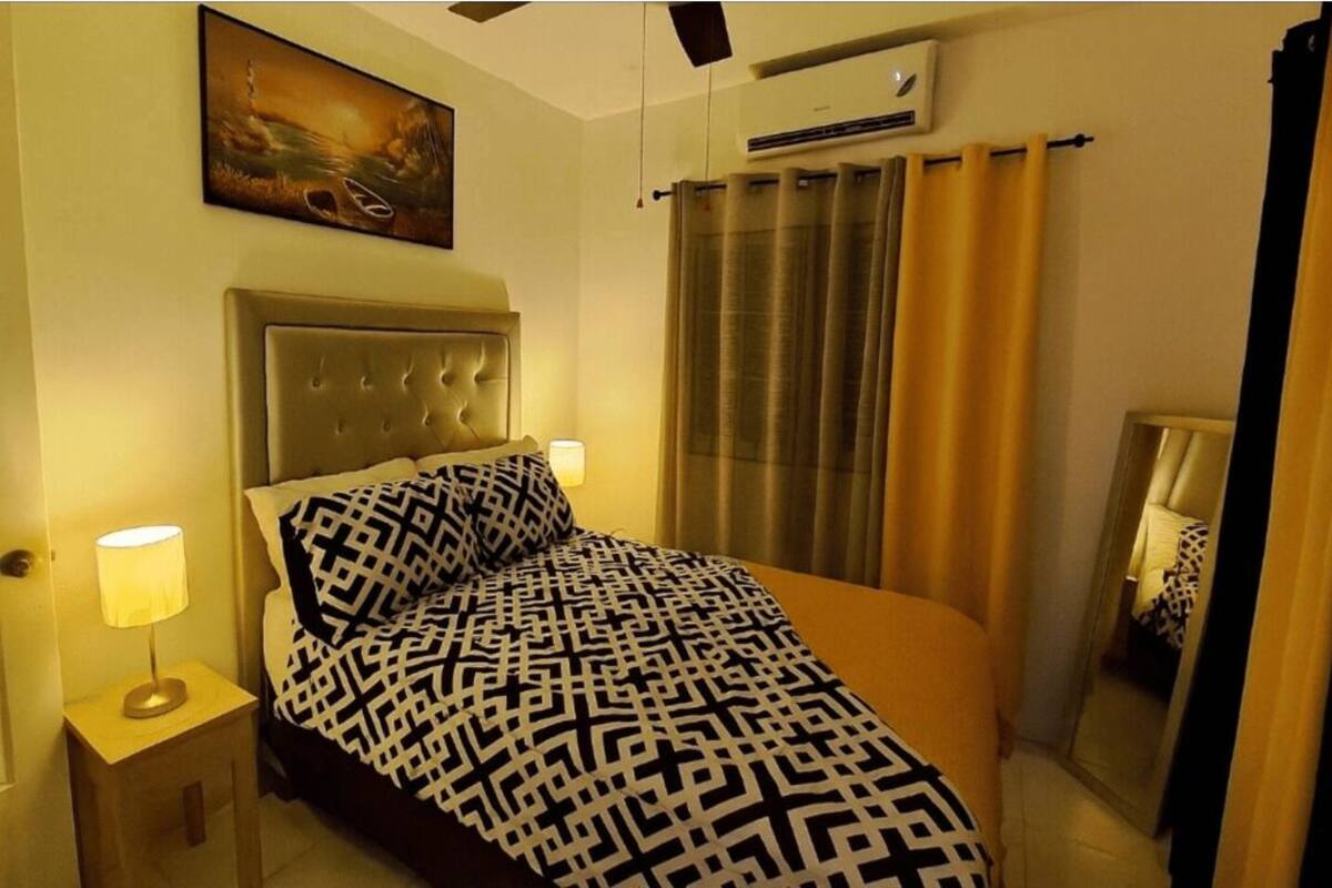 Camera d'albergo con un letto, un comodino con una lampada, un quadro appeso al muro e un condizionatore d'aria.