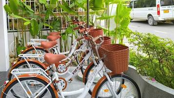 A row of vintage bicycles with baskets, parked in an outdoor area with greenery and a white van in the background.
