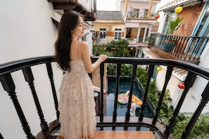 A woman standing on a balcony with a pool and plants visible below.