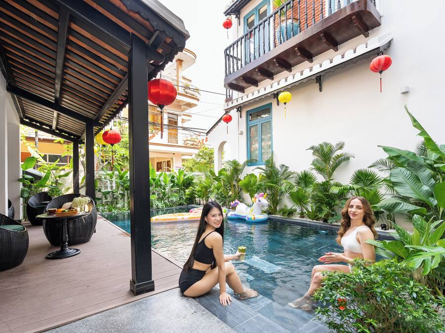 A poolside area with a covered seating area, a pool, and surrounding greenery.