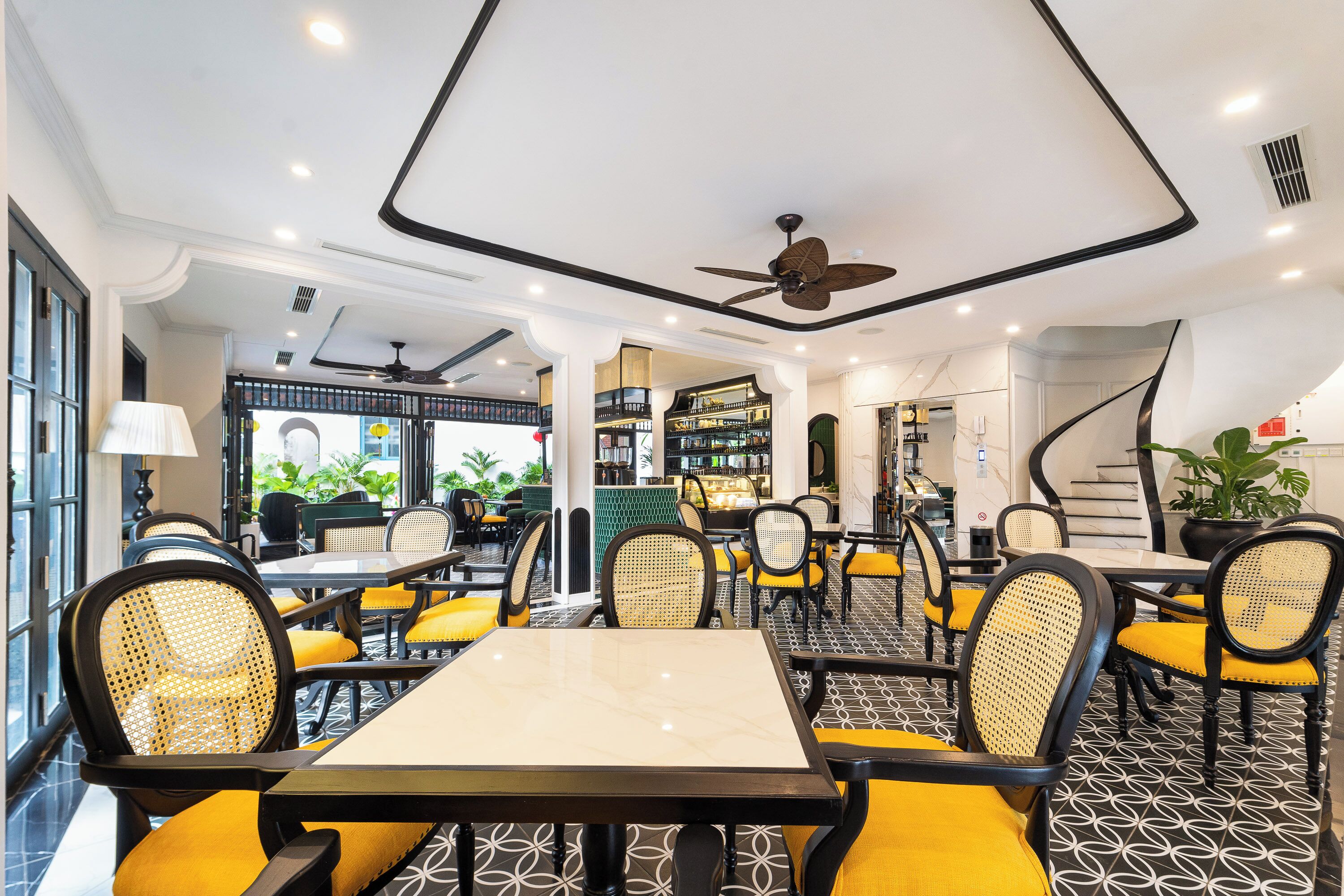 A modern restaurant with high ceilings, black and white patterned flooring, yellow cushioned chairs, and a central dining table.