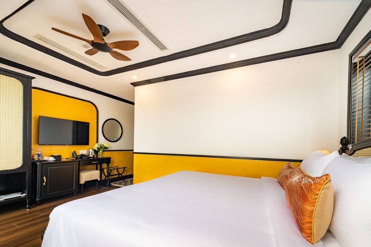 Una habitación de hotel con una cama, un escritorio, una silla, un televisor y un ventilador de techo.