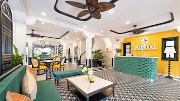 A hotel lobby with a reception desk, seating area, and ceiling fans.