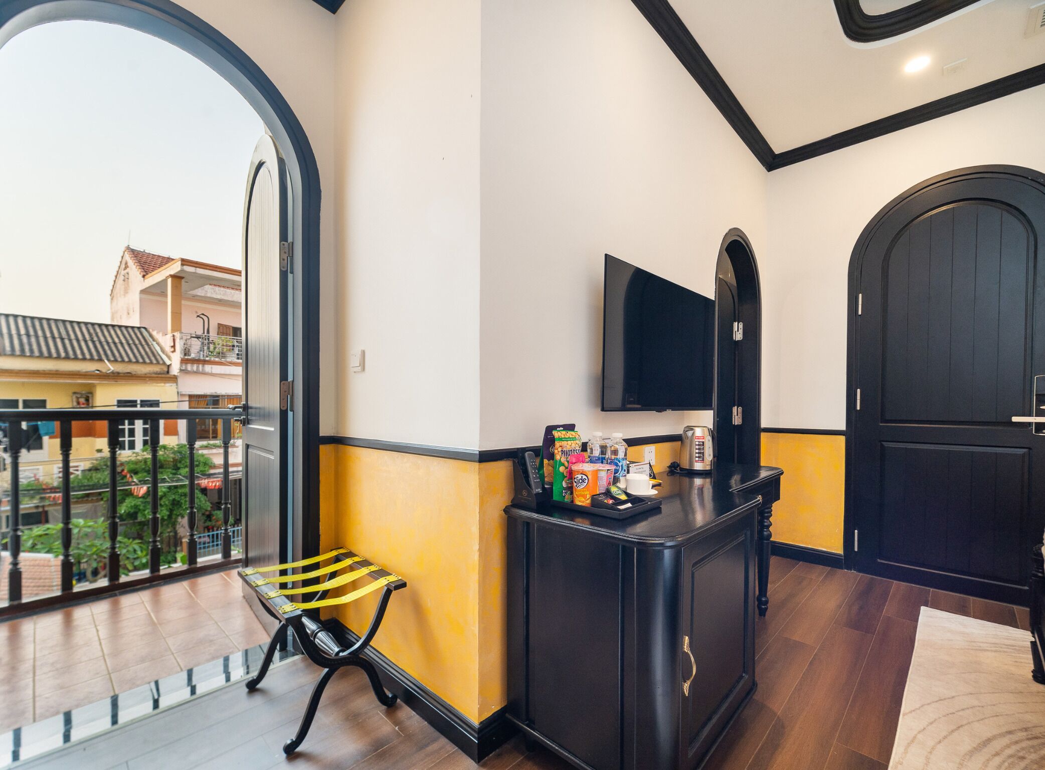 A hotel lobby with a large arched window, a reception desk with a flat-screen TV, a small seating area, and a door.