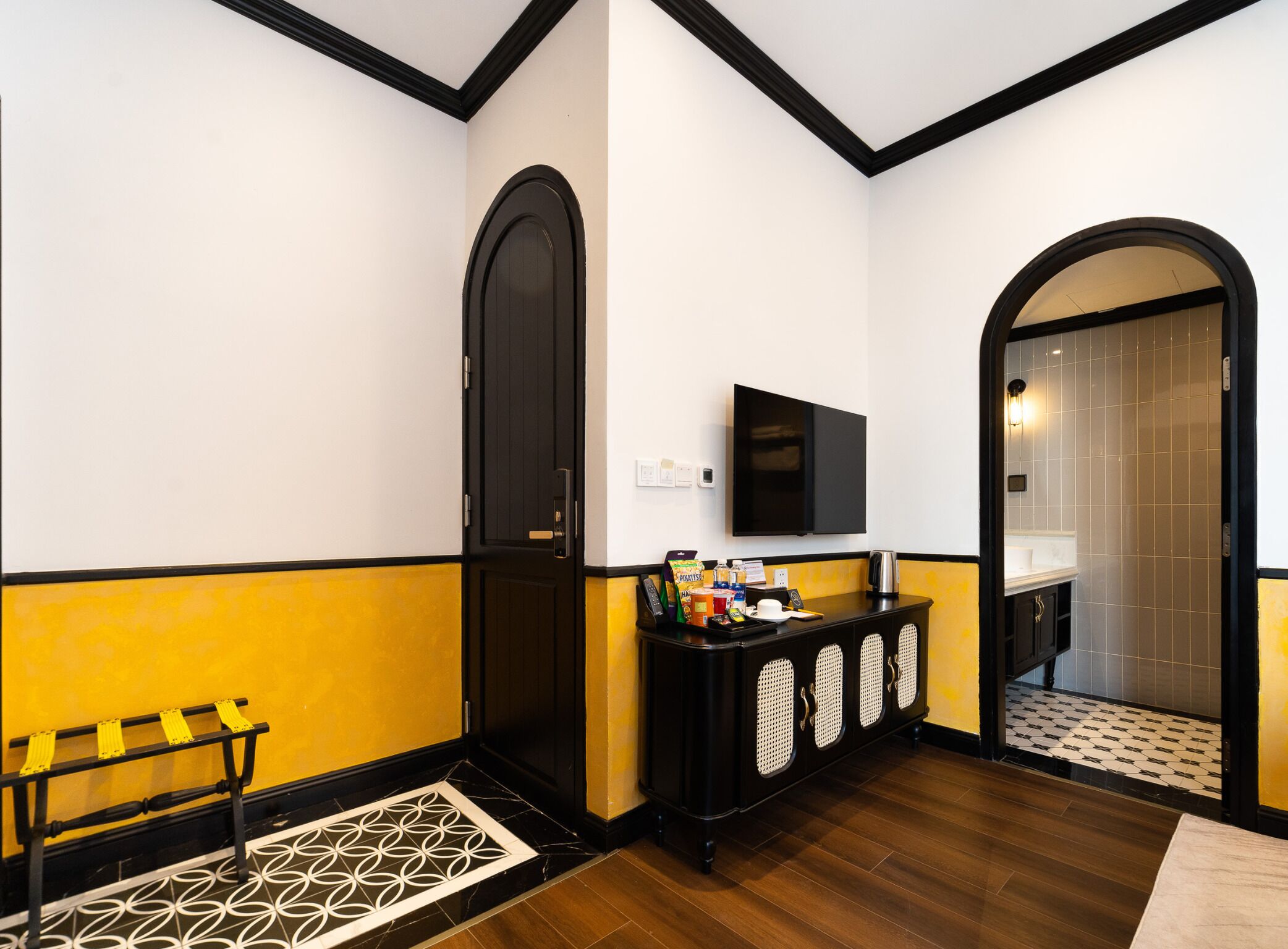 A hotel lobby with a black and yellow color scheme, a reception desk, a television, and a bathroom visible through an archway.
