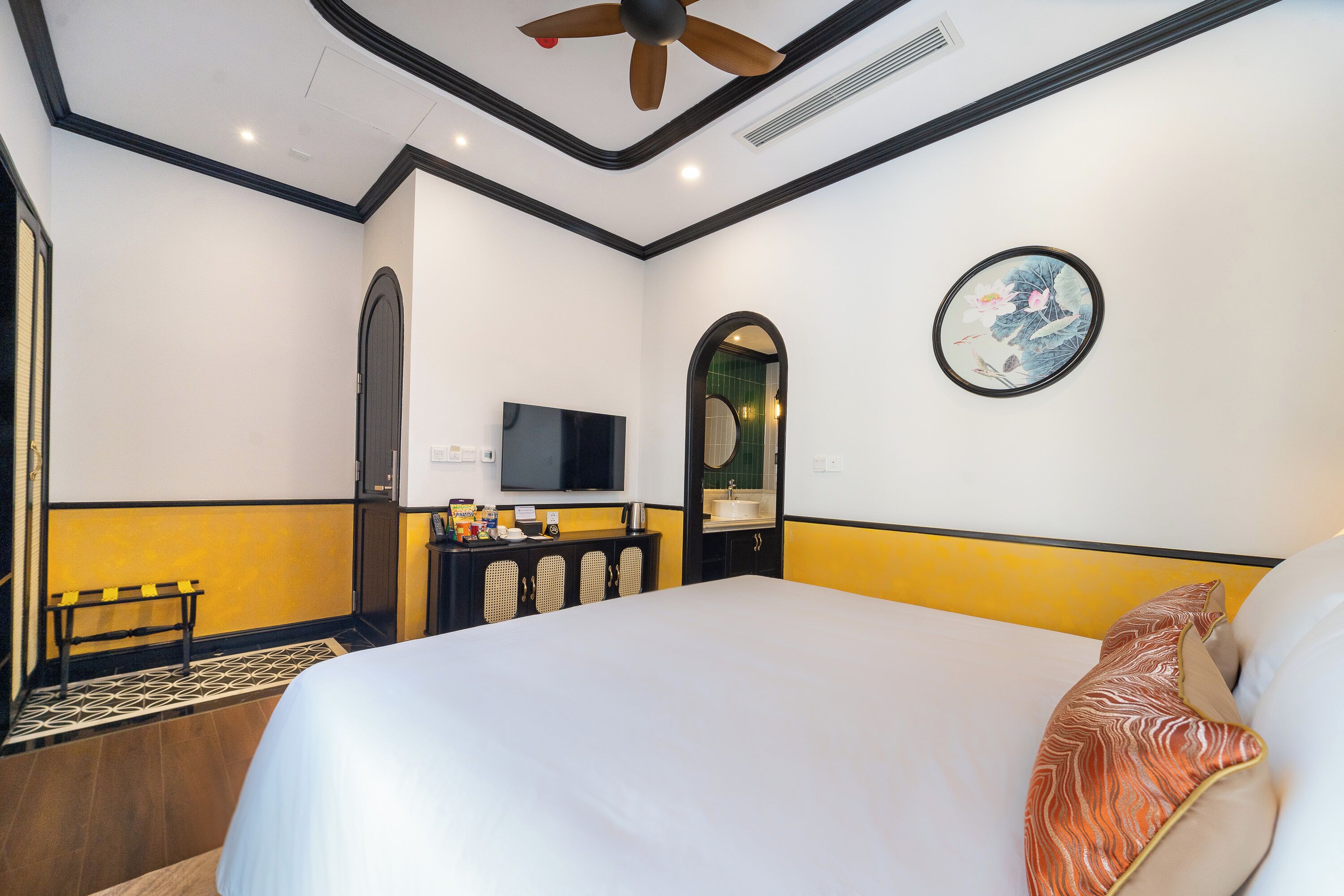 A hotel room with a large bed, a television, a small desk with a sink, and a decorative wall piece.