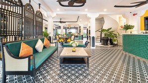 Un vestíbulo de hotel con un sofá verde, una mesa de centro, suelo estampado y ventiladores de techo.