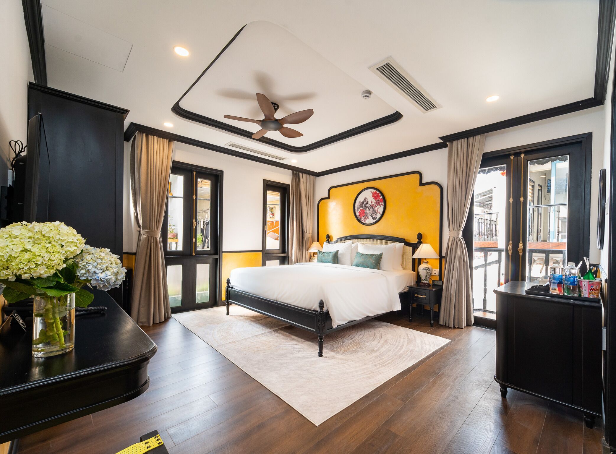 A hotel room with a bed, a desk, a chair, a ceiling fan, and a window.