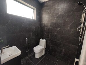 Ein modernes Badezimmer mit dunklen Marmorwänden, einer weißen Toilette, einem Waschbecken und einer Dusche.