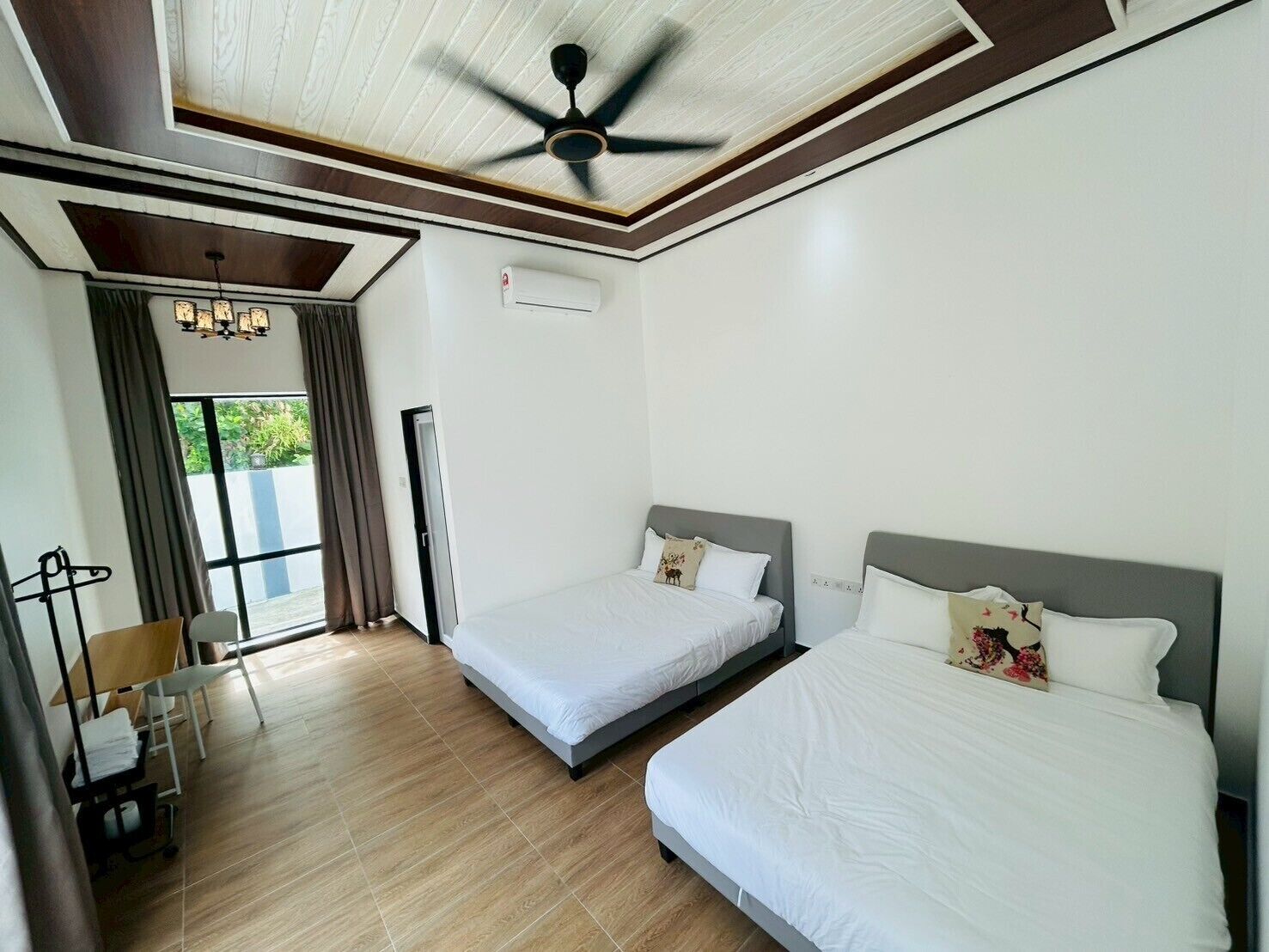 A hotel room with two beds, a ceiling fan, a window with curtains, and a desk with a chair.