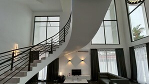 Un'ampia zona giorno con una scalinata a forma di curva, un'area salotto con divani, un tavolino da caffè e una TV a schermo piatto.
