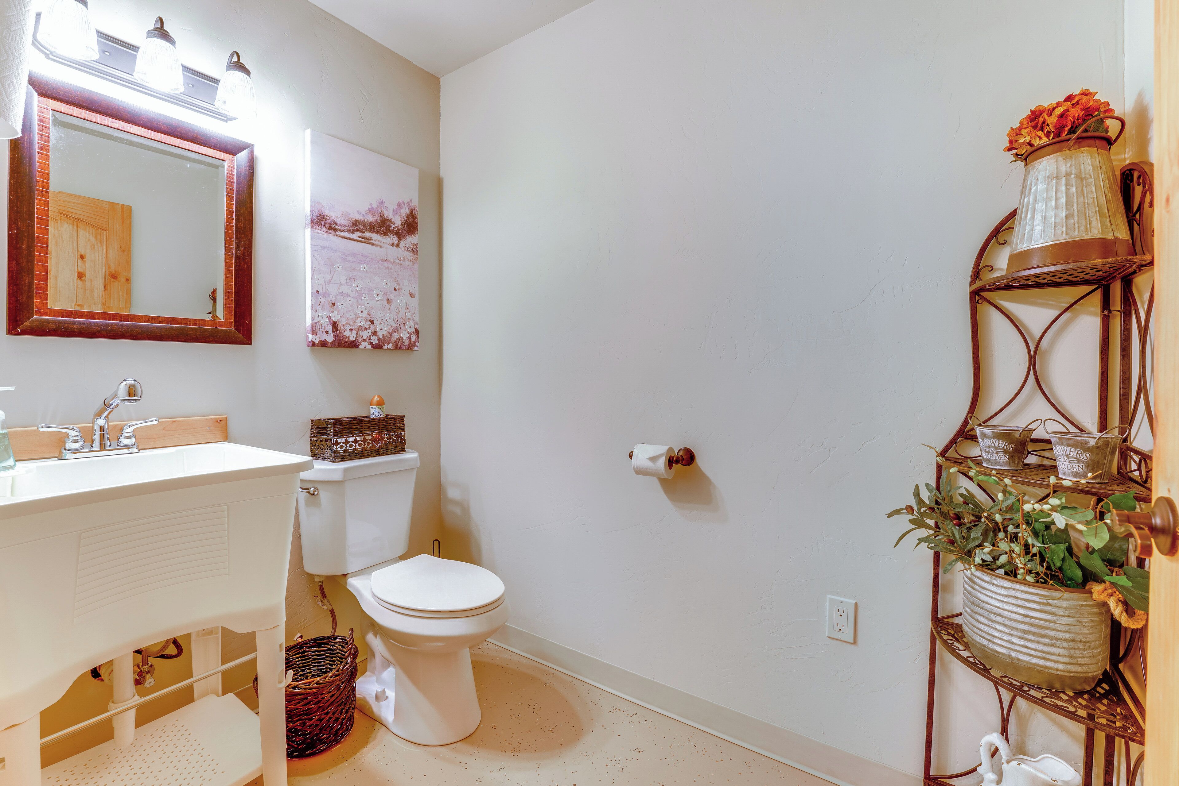 Une salle de bain avec un lavabo blanc, des toilettes, un miroir et une étagère décorative pour plantes.