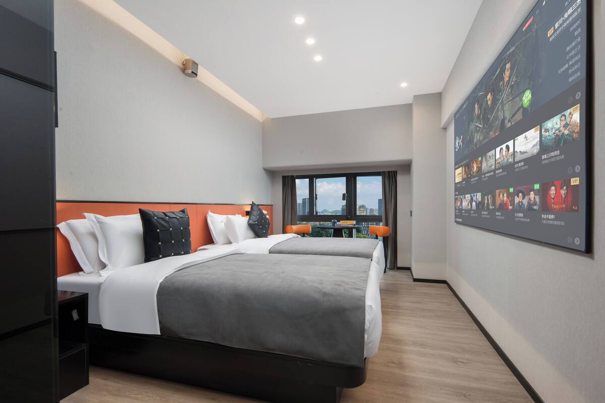 A modern hotel room with a large bed, a desk, and a TV displaying a movie.