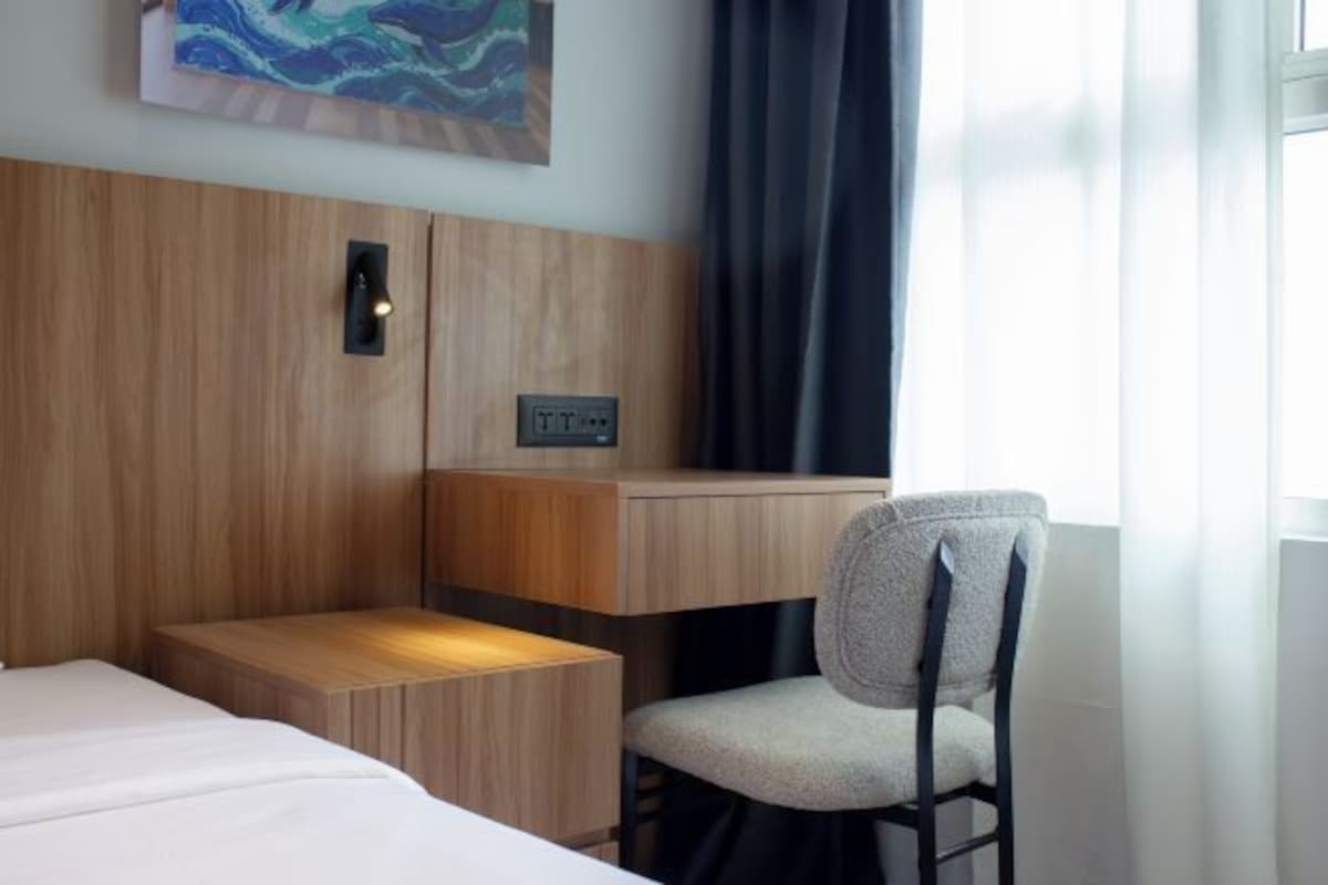 Habitación de hotel con cama, escritorio y silla, una lámpara de pared y un cuadro.