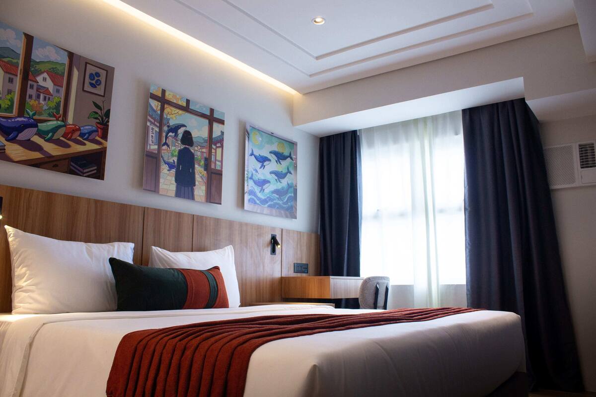 A hotel room with a large bed, a desk, and artwork on the walls.