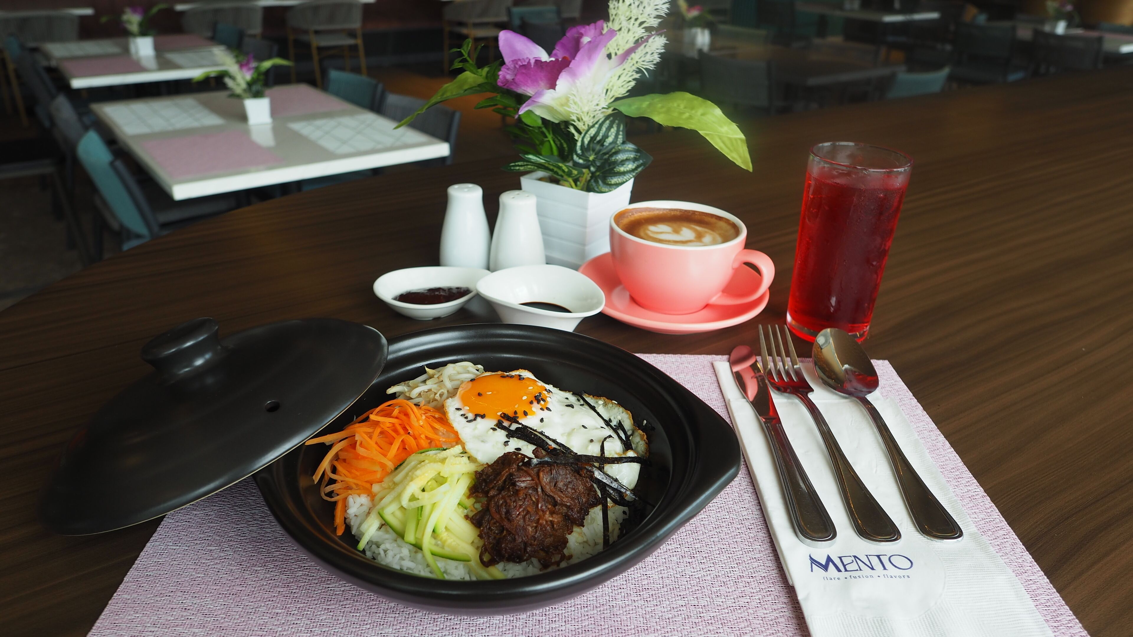 A meal with rice, vegetables, and meat, a cup of coffee, a glass of red drink, and a flower arrangement on a table.