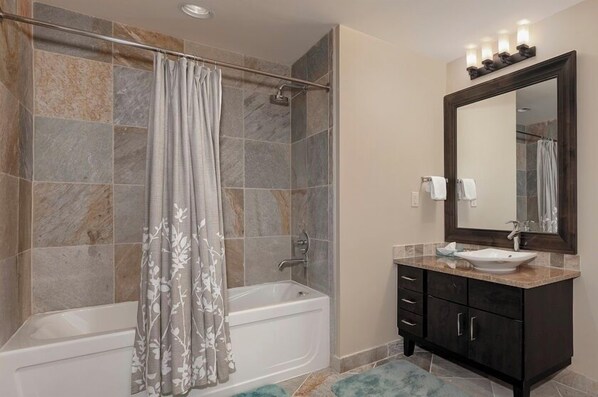 Une salle de bain équipée d’une baignoire, d’une douche, d’un meuble-lavabo et d’un grand miroir.