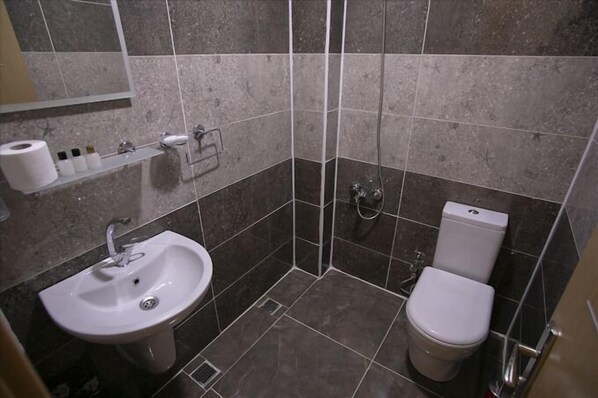 Un baño pequeño y moderno con lavamanos, inodoro y ducha blancos.