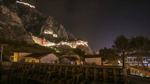 A night view of a mountain with illuminated buildings, wooden benches, and a small structure with a thatched roof. - SEMAY OTEL (Amasya)