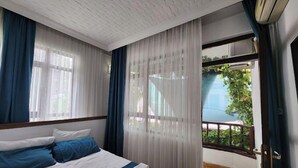 A hotel room with a bed, curtains, and a view of greenery outside. - SEMAY OTEL (Amasya)