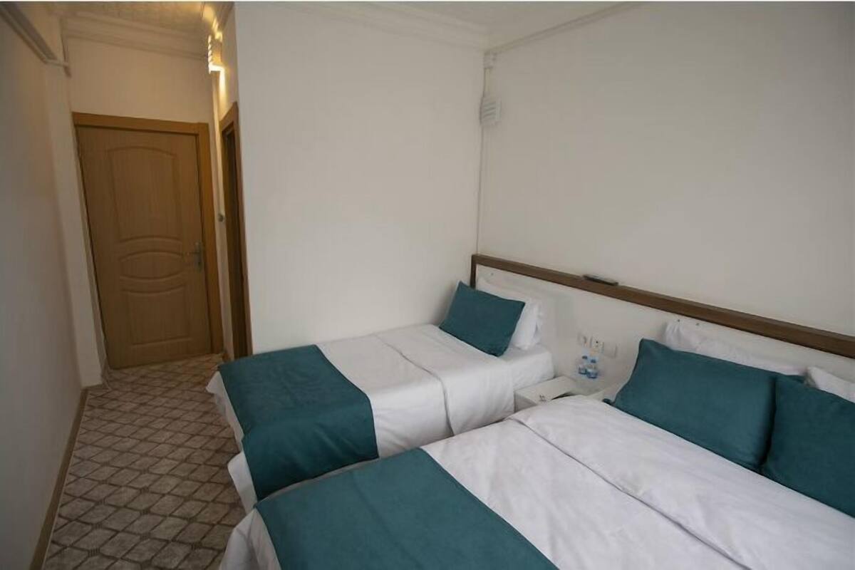A hotel room with two single beds, a wooden door, and a tiled floor.