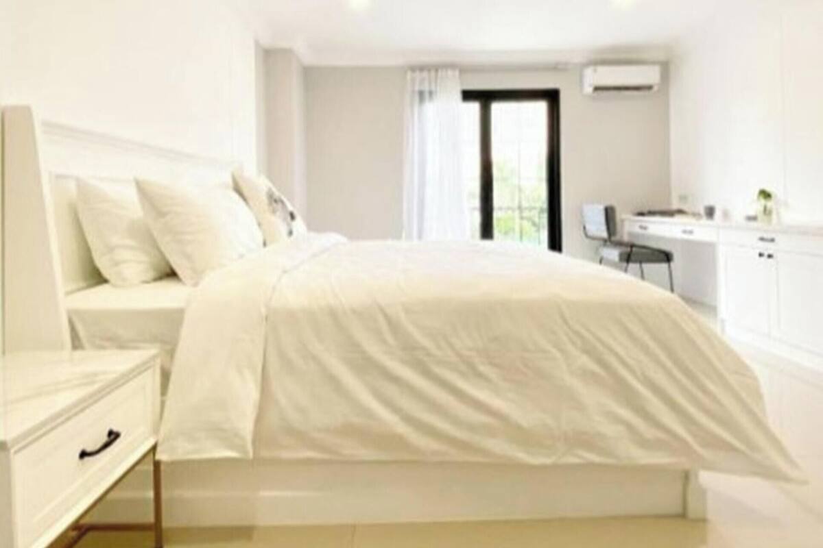 A modern bedroom with a bed, bedside table, and a view of a kitchen area.