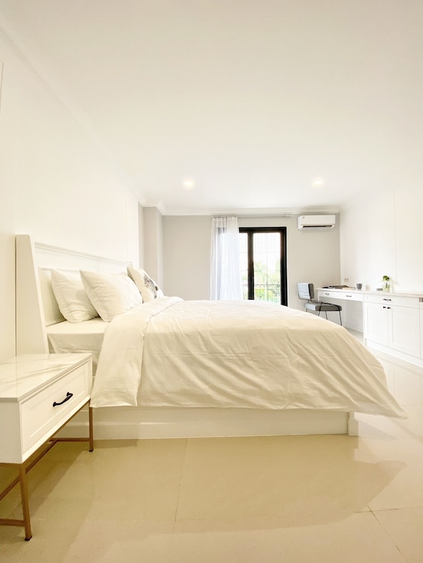 A bedroom with a bed, a bedside table, a desk, and an air conditioning unit. - Loewy's Home Jakarta (Jakarta)