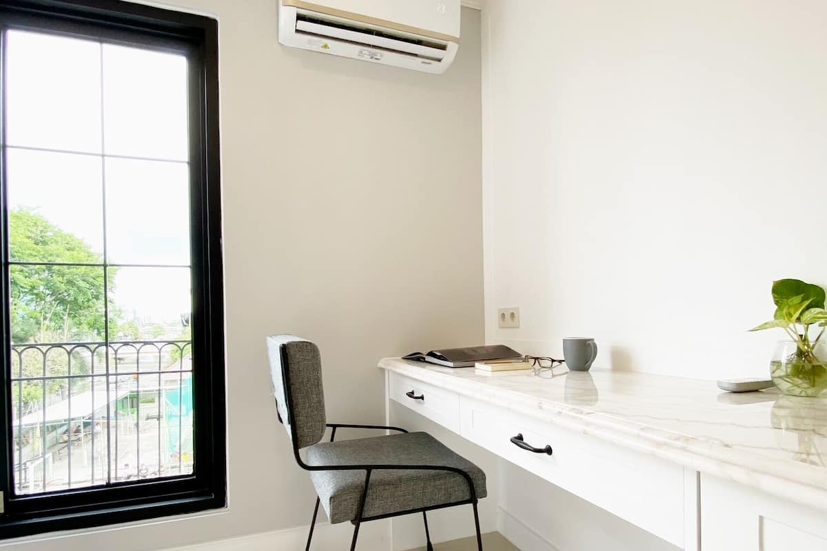 A modern office space with a large window, a desk with a chair, and an air conditioning unit.