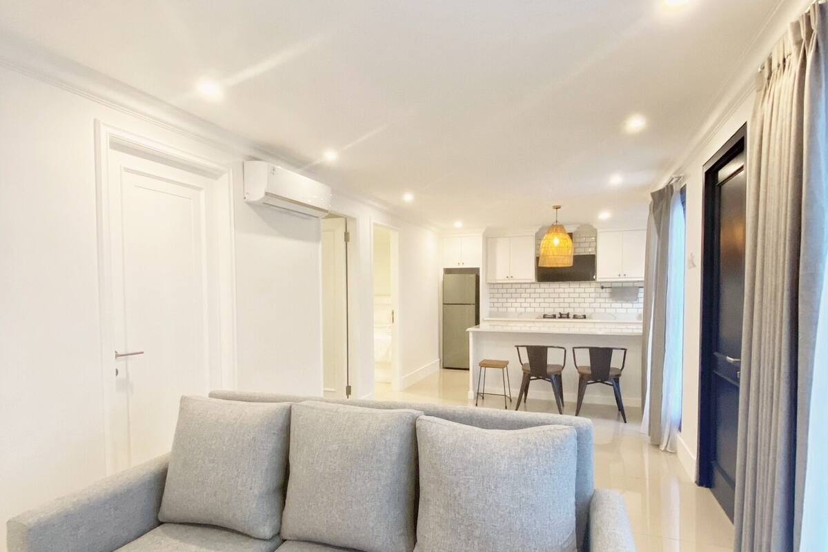 A modern living room with a grey sofa, a kitchen in the background, and a dining area.