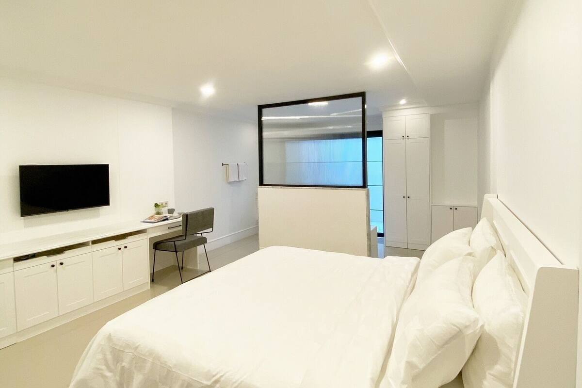 A modern bedroom with a large bed, a desk, and a TV.