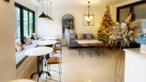 A modern living room with a fireplace, a dining area with round tables, and a Christmas tree. - Loewy's Home Jakarta (Jakarta)