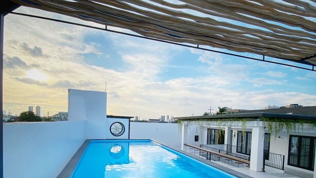 A rooftop swimming pool with a pergola overhead, surrounded by a white wall and a cityscape view. - Loewy's Home Jakarta (Jakarta)