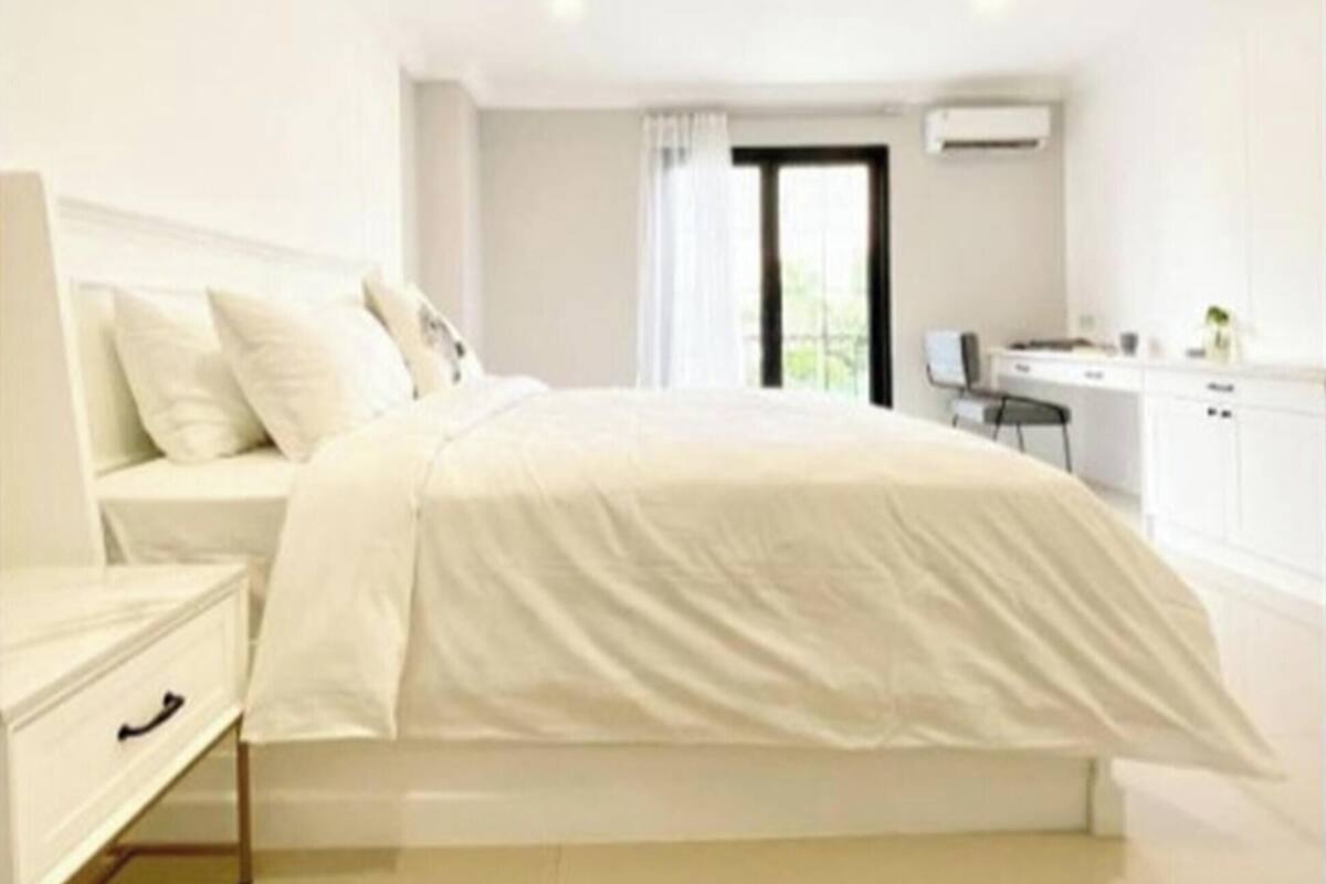 A modern bedroom with a bed, bedside table, and a view of a kitchen area.