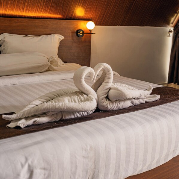 Een netjes opgemaakt bed met twee handdoeken in de vorm van een zwaan, een houten hoofdbord en een wandlamp.