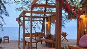 Eine Holzterrasse mit Bänken und Tischen, mit Blick auf einen Strand und das Meer.