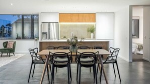 A modern kitchen with a dining area, featuring a wooden table and chairs, a large window, and a built-in oven. - Birkenhead Point Beauty - quiet family home with amazing views. (Auckland)