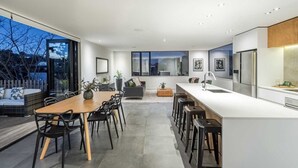 A modern kitchen with a central island, bar stools, and a dining area with a wooden table and chairs. - Birkenhead Point Beauty - quiet family home with amazing views. (Auckland)