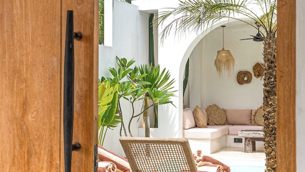A wooden door opening to a patio with a wicker chair, a sofa, and potted plants. - the macan Bingin (Pecatu)