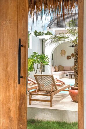 A wooden door opening to a patio with a wicker chair, a sofa, and potted plants. - the macan Bingin (Pecatu)