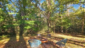 An outdoor seating area with metal chairs and a fire pit in a forest setting.
