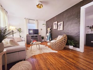 Una sala de estar con televisión, sofá, sillón de mimbre y chimenea.