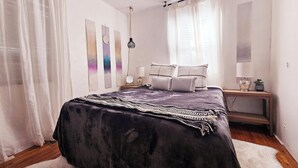 A bedroom with a large bed, a bedside table with a lamp, and a small plant.