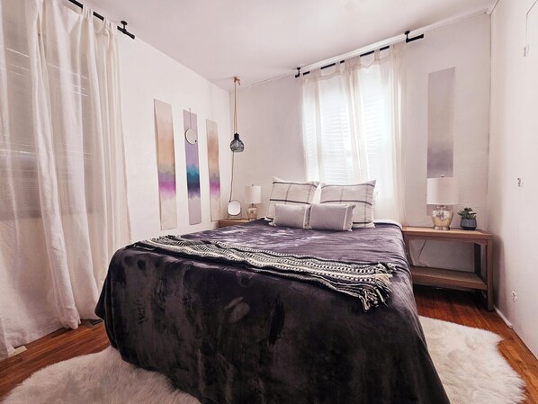 Un dormitorio con una cama grande, una mesita de noche con una lámpara y una planta pequeña.