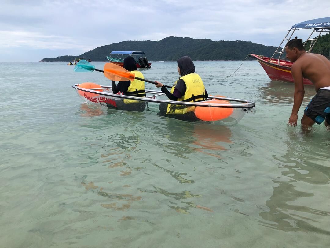 Two people in a small boat with life jackets, a larger boat in the background, and a hilly landscape.