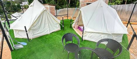 Un área de camping con dos tiendas de campaña blancas, una mesa con sillas y suelo cubierto de césped.