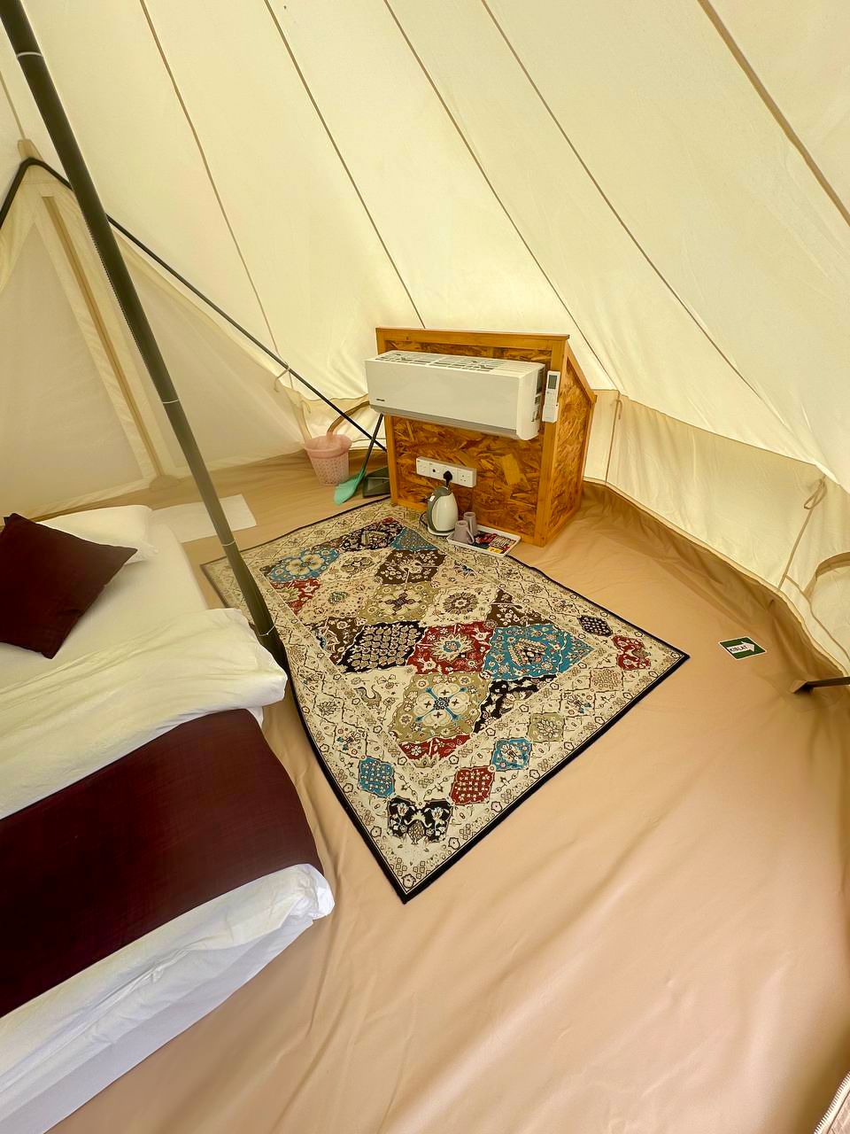 Une tente avec un lit, une petite armoire en bois et un tapis à motifs.