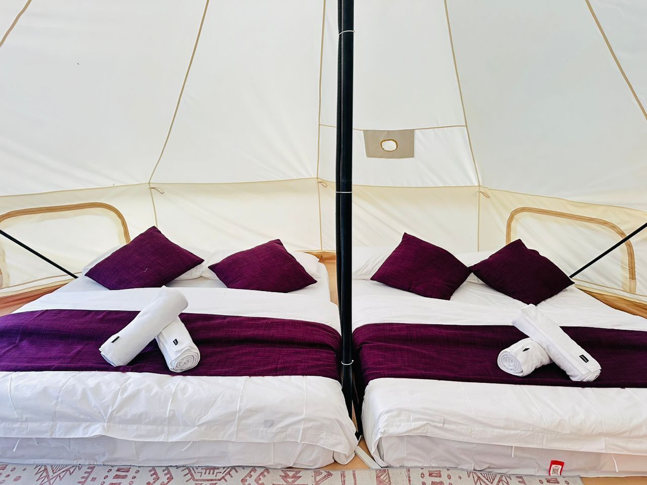 Una habitación tipo tienda de campaña con dos camas, cada una con ropa de cama blanca y detalles morados.
