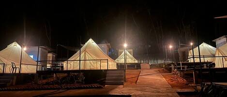 A row of white tents illuminated by overhead lights, arranged in a linear fashion with a central pathway leading through them.