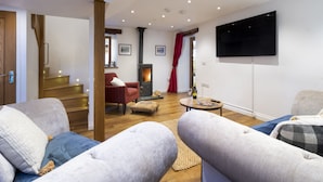Een moderne woonkamer met een open haard, comfortabele zitplaatsen, een flatscreen televisie en een trap naar een hoger niveau.
