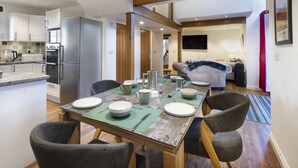 Een eetgedeelte met een houten tafel voor vier personen, omringd door stoelen. Achtergrond toont een keuken met moderne apparatuur.